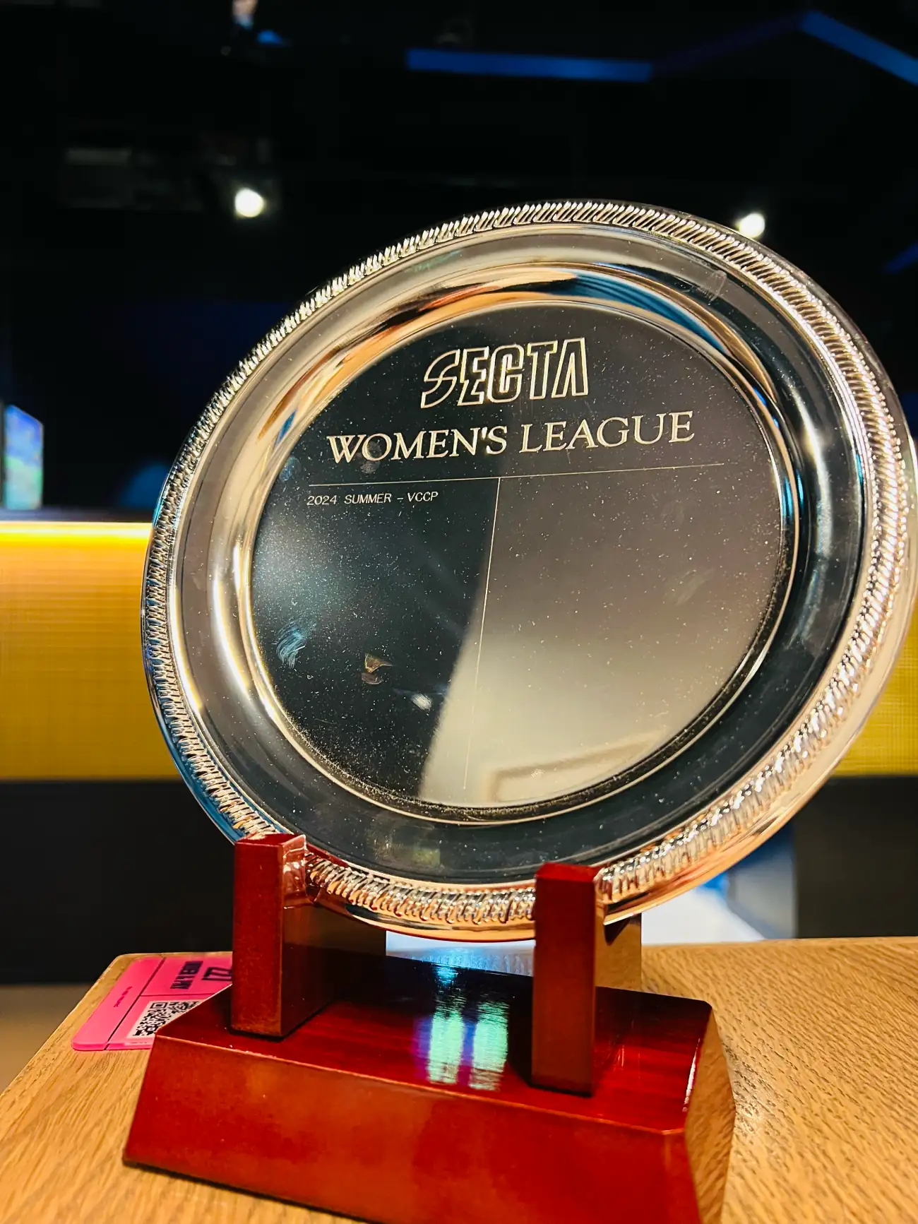 Close-up of an engraved silver trophy plate reading Secta Women's League, 2024 Summer, mounted on a wooden stand.