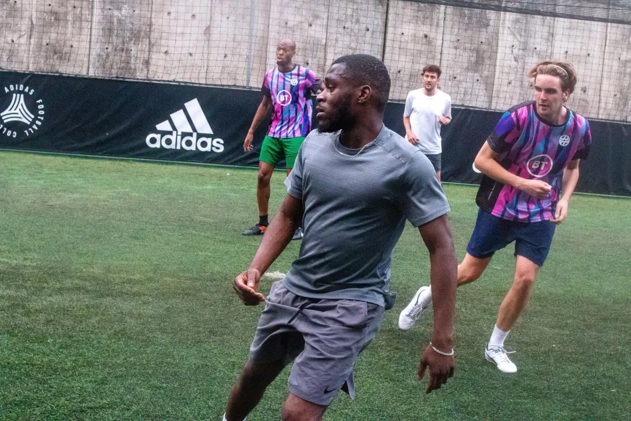 Players in purple and pink kit sprinting across a five-a-side pitch in front of Adidas-branded boarding.