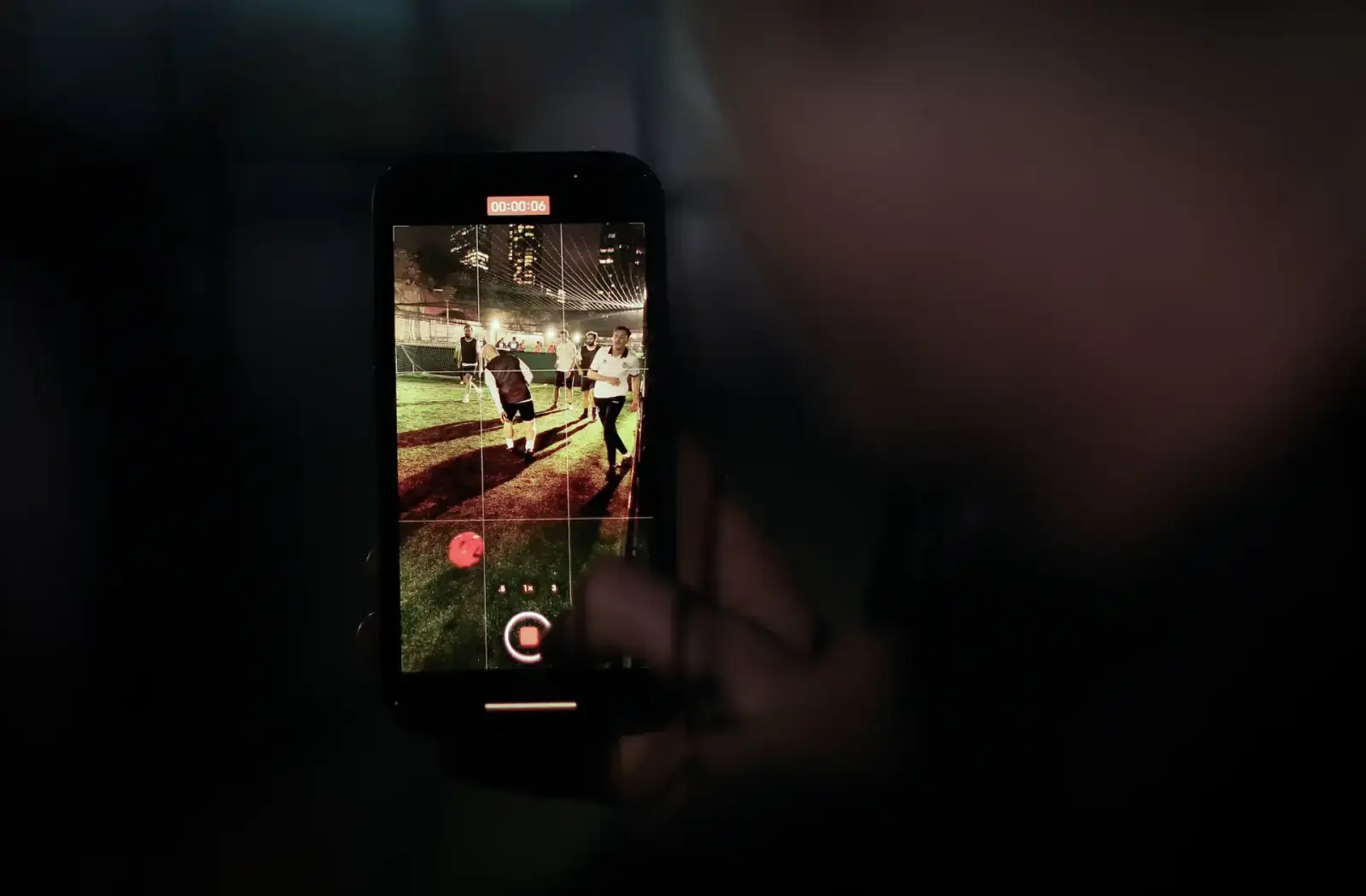 A phone screen recording a five-a-side match in progress, London high-rises glowing in the background as players run for the ball.